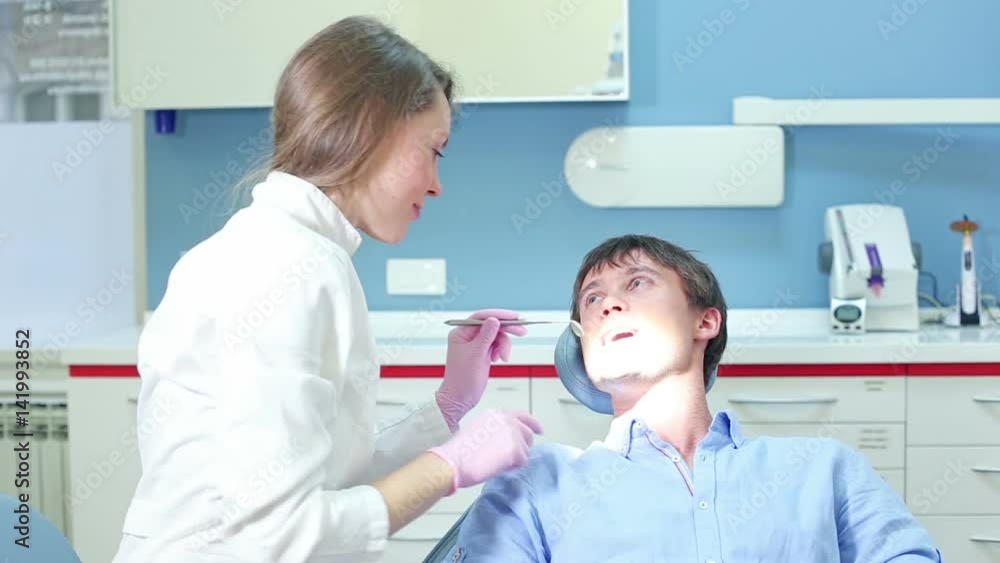Beautiful female dentist doing routine check up to young attractive male patient, graded Beautiful female dentist doing routine check up to young attractive male patient, graded