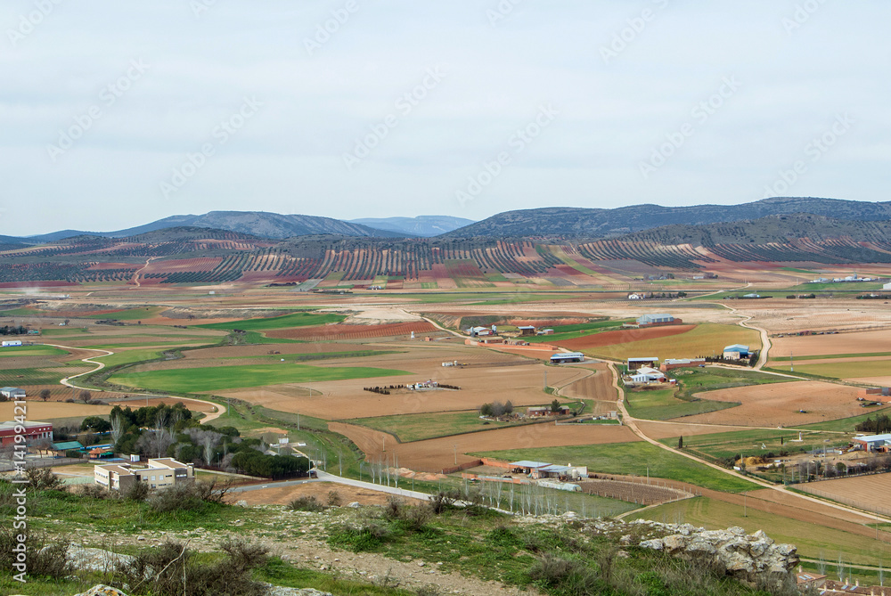 A view from observation deck to fields, farms and mountains near Consuegra town at spring cloudy day, Castilla La Mancha, Spain. A view from observation deck to fields, farms and mountains near Consuegra town at spring cloudy day, Castilla La Mancha, Spain.
