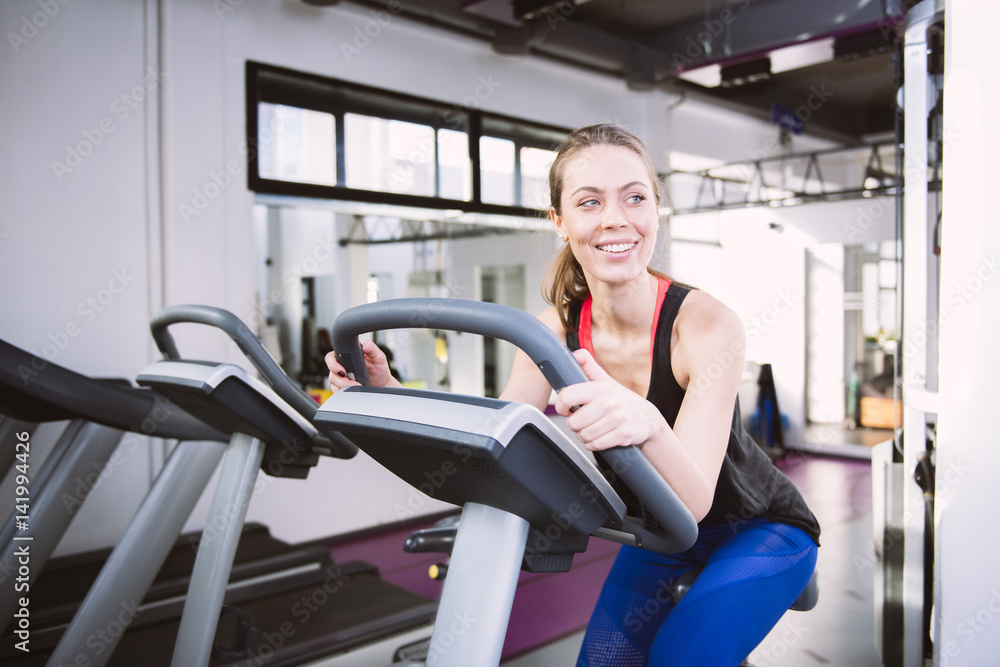 Smiling woman riding an exercise bike in gym Smiling woman riding an exercise bike in gym