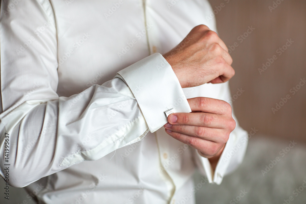 Preparing for wedding. Groom buttoning cufflinks on white shirt before wedding. Groom's clothes. Close up.
