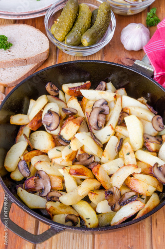 Fried potatoes with mushrooms in a pan on a wooden background