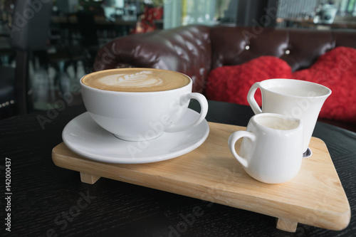 White cup of coffee on wooden table in the coffee shop.