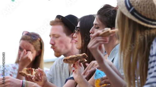 Group of young friends enjoying at a party while eating pizza