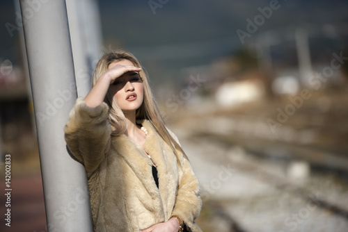 Pretty young woman standing at the railway platform wear sheep jacket and black long skirt