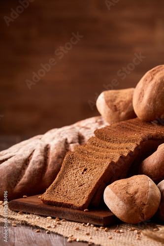 Freshly baked bread loaves on burlap on wooden table with brown blurred background. Texture closeup bakery products