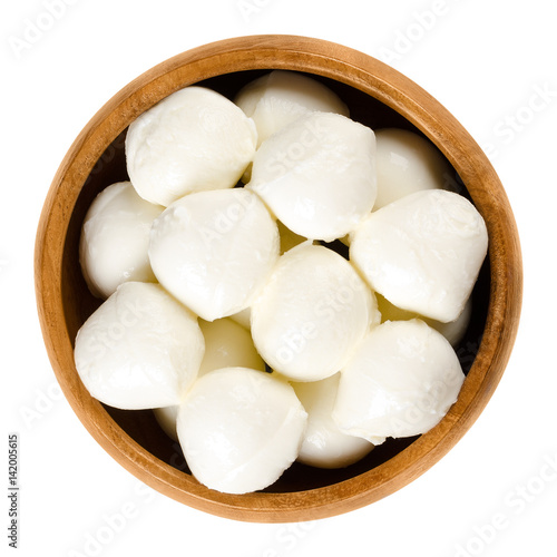 Small mozzarella balls in wooden bowl. Fresh white southern Italian cheese made from milk by the pasta filata method, also called bambini bocconcini. Macro food photo close up from above over white.