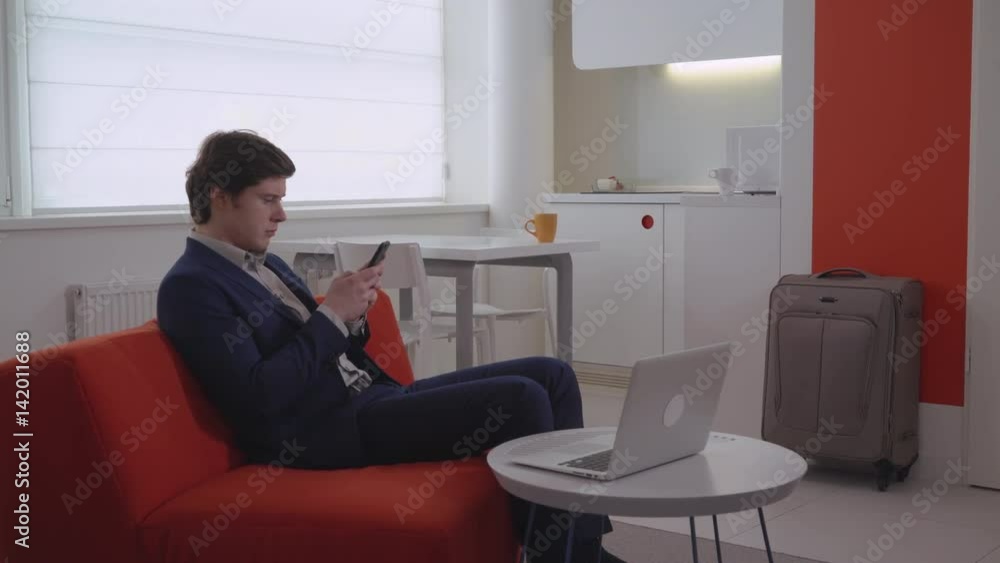 Attractive guy use app on cell in flat. Businessman use application on smart phone chatting or checking mail. Young caucasian guy in modern apartment with white interior messaging on smartphone. Attractive guy use app on cell in flat. Businessman use application on smart phone chatting or checking mail. Young caucasian guy in modern apartment with white interior messaging on smartphone.