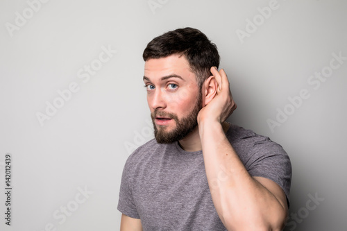 Closeup portrait a man placing hand on ear listening carefully isolated on gray wall background.