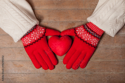 female hands in gloves holding heart shaped toy on the wonderful brown wooden background