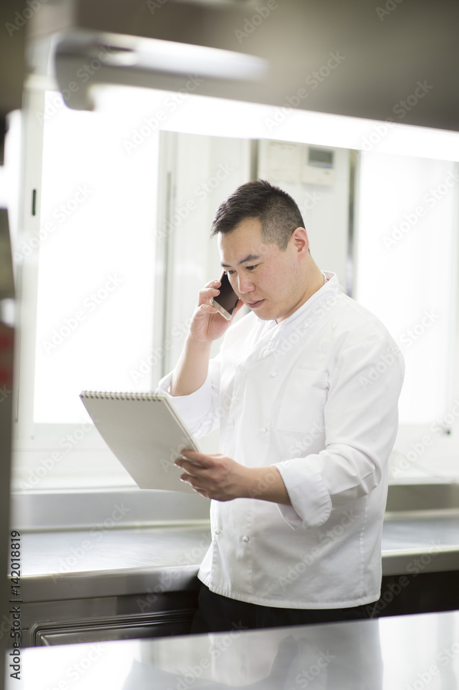 Fototapeta premium Chinese cook speaks with smartphone and notebook