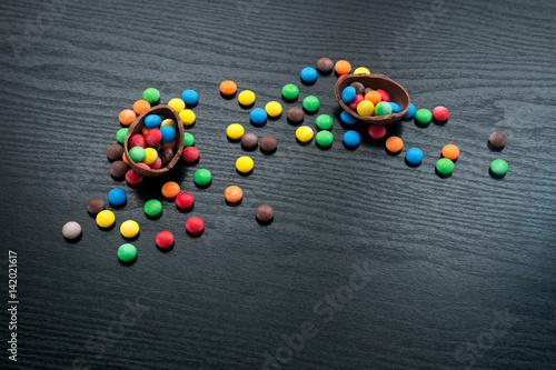 Chocolate easter eggs, multi-colored sweets candy on a textured black wooden background. The concept of a holiday and a happy Easter. With space for text