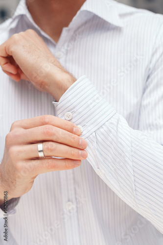 Man buttons cuff-link on French cuffs sleeves luxury white shirt. Close up of a businessman showing a shirt cuff.