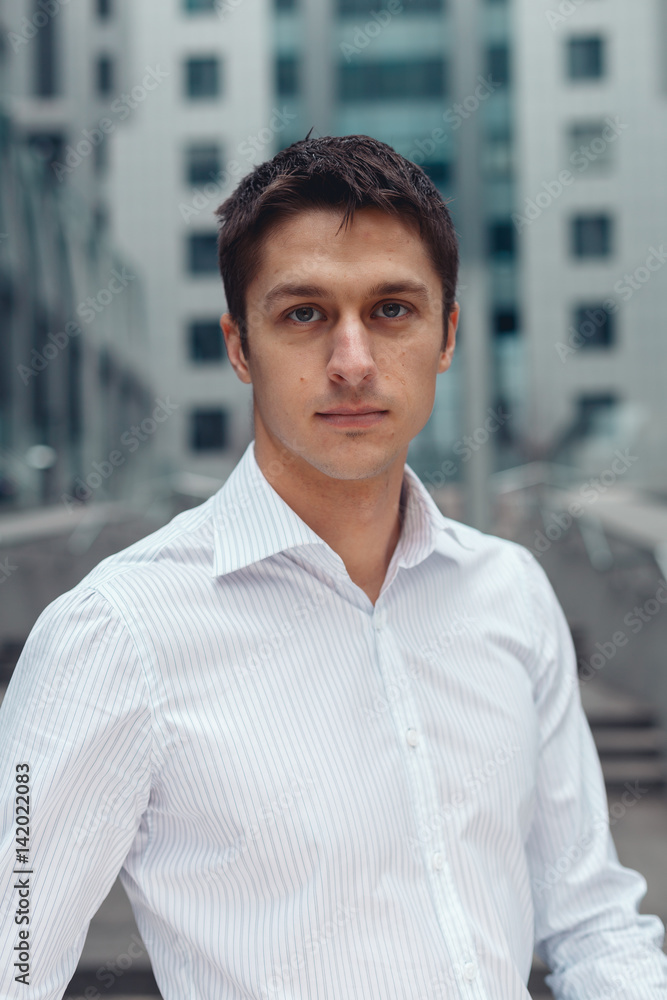 Obraz premium Smiling relaxed businessman standing in an urban square. Young business man looking at camera and posing.
