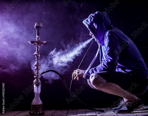 a man smokes a hookah on a black background, beautiful lighting photo