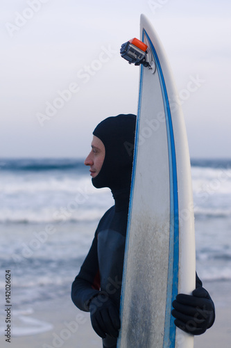 Wet surfer with surfboard standing on the sand on the beach.  photo