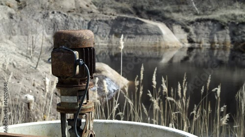 A rusty old vertical pump or sump pump sitting abandoned in front of a pond contaminated with minerals that have leached into the water which is an environmental concern. photo