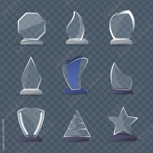 Transparent glass awards of various shapes and materials stand.