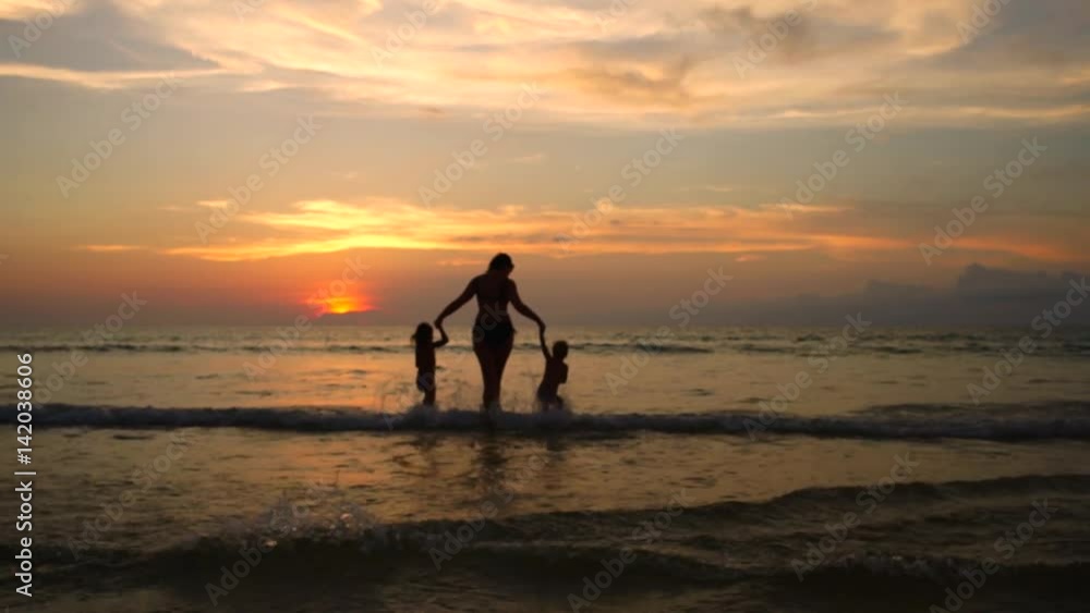 Happy mother with two baby daughters having fun on the ocean at sunset Happy mother with two baby daughters having fun on the ocean at sunset