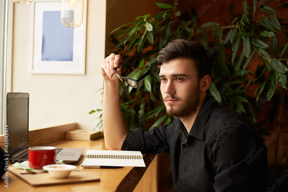 Thoughtful hipster man thinking in cafe about new startup, how increase income of his business. Dark skin male look to the window to find new idea. Coffee break in lunch time. Thoughtful hipster man thinking in cafe about new startup, how increase income of his business. Dark skin male look to the window to find new idea. Coffee break in lunch time.
