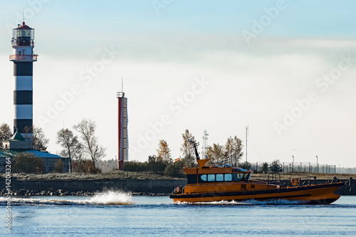 Orange pilot ship sailing past the lighthouse in Riga