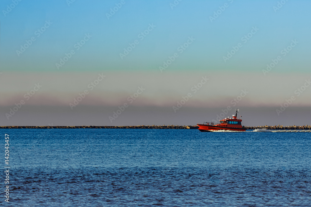 Red pilot ship moving past the breakwater dam in Riga, Europe