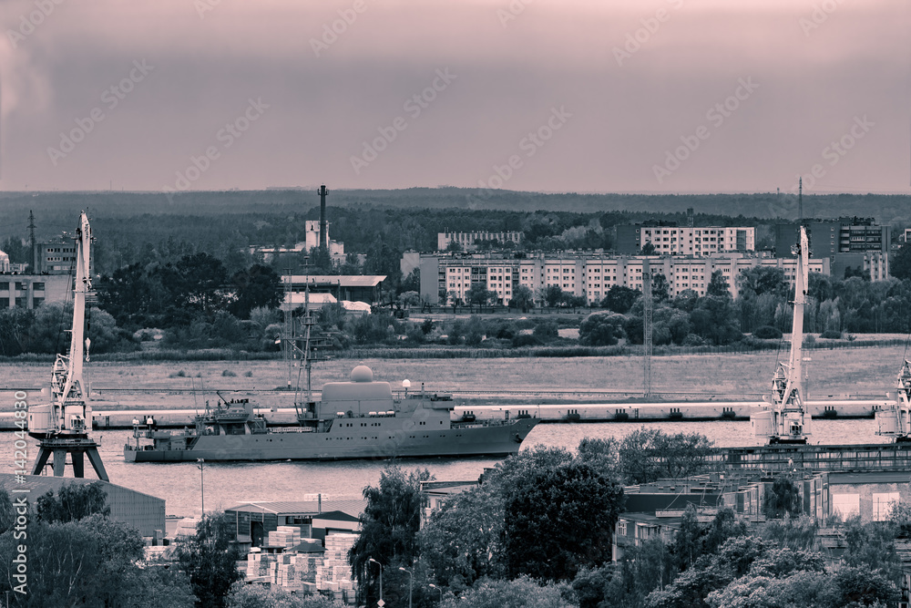 Military ship sailing past the cargo port in Riga, Latvia