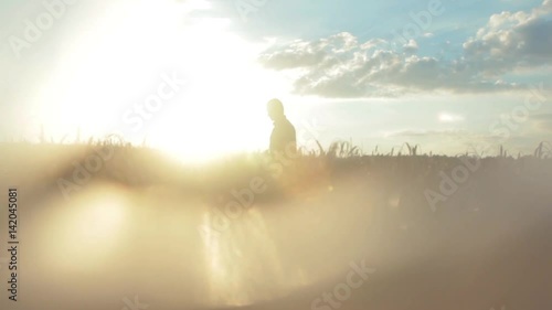 The man is walking across the field at sunset, in the sun