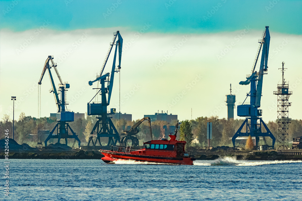 Red pilot ship moving past the cargo cranes