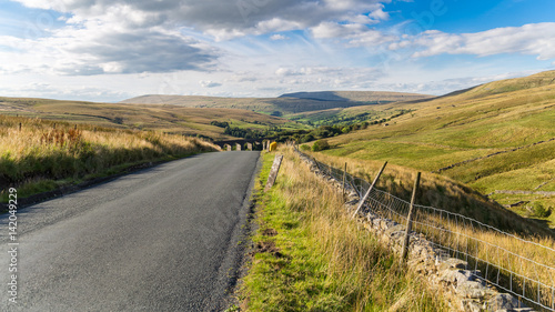 Country road in the Yorkshire Dales with Dent Head Viaduct in the background, between Cowgill and Gearstones, North Yorkshire, UK