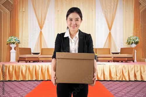 A young woman carrying a box with smile in a conference hall photo