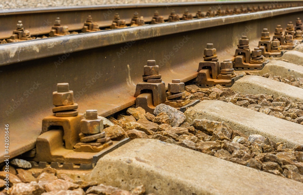 Background picture: steel rails which run diagonally from lower left corner to the upper right corner close-up visible rusty fasteners, nuts, bolts, stones, concrete sleepers Background picture: steel rails which run diagonally from lower left corner to the upper right corner close-up visible rusty fasteners, nuts, bolts, stones, concrete sleepers