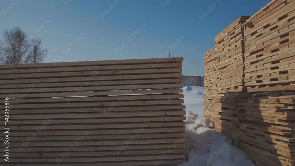 Wood construction and the production of laminated veneer lumber. Wooden boards neatly stacked in neat rows. Boards for building standing on the street on a background of blue sky and white snow. Wood construction and the production of laminated veneer lumber. Wooden boards neatly stacked in neat rows. Boards for building standing on the street on a background of blue sky and white snow.