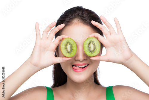 Tropical fruits. Healthy eating. Charming young asian woman holding fresh juicy kiwi and smiles. Green background.