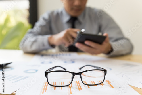 eyeglasses on desk wtih businessman analyzing report on chart with calculator