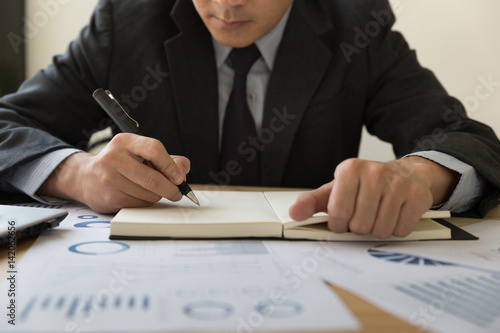 Businessman analyzing charts and graphs and taking notes. © 88studio