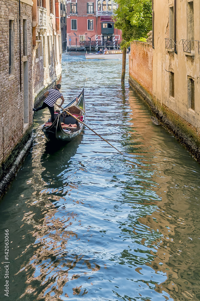 Gondolier leans one leg on a wall of the Rio San Falice to give himself a boost towards the Grand Canal of Venice, Italy