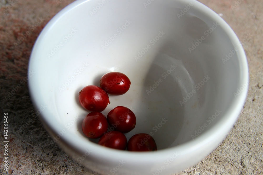 Closeup of raw coffee cherries in a small white cup Closeup of raw coffee cherries in a small white cup