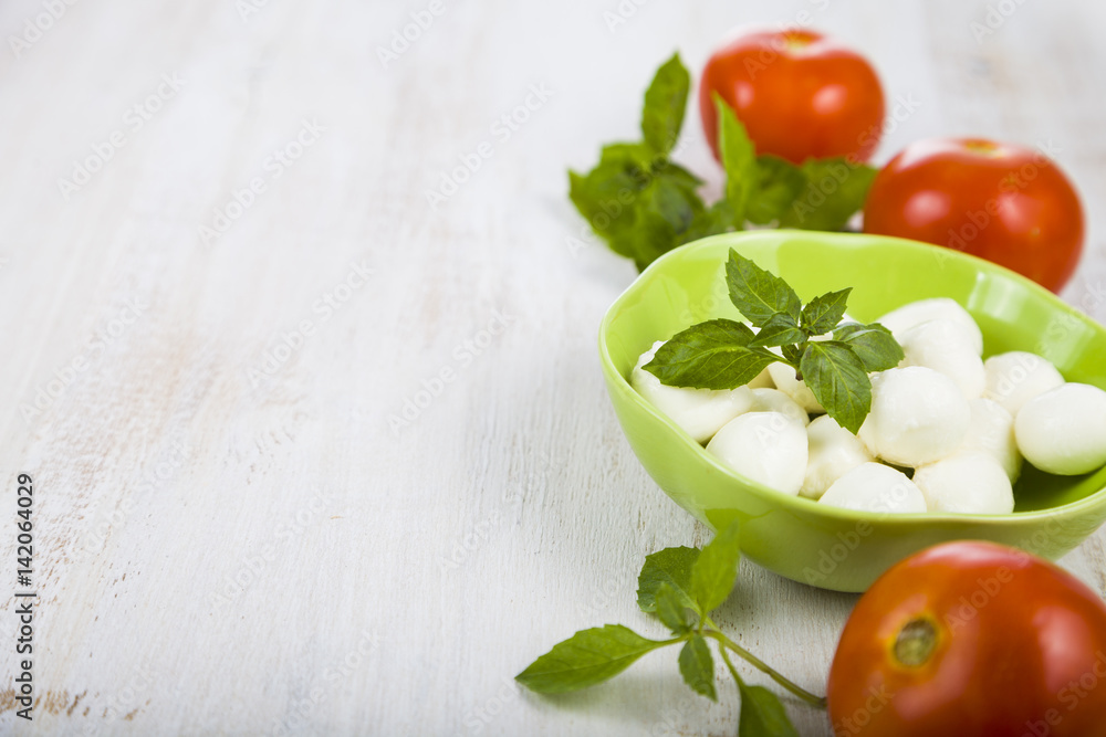 Mozzarella in a green plate on a wooden table. Mozzarella balls with basil leaves and tomato on a wooden board. Mozzarella in a green plate on a wooden table. Mozzarella balls with basil leaves and tomato on a wooden board.