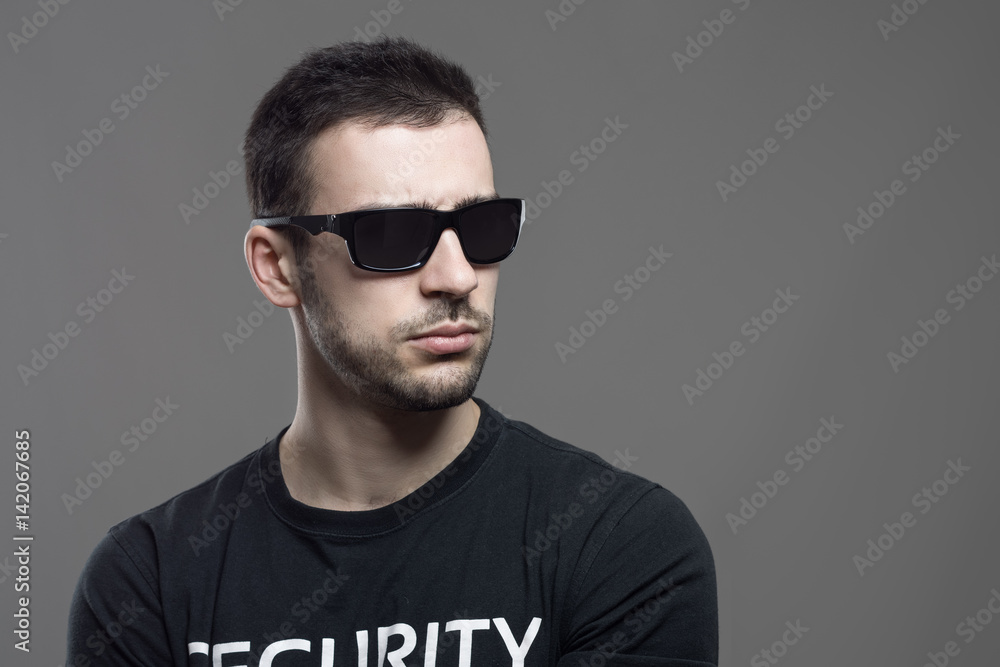 Macho tough security agent wearing sunglasses looking away at copyspace. Atmospheric contrasty portrait over gray studio background. Macho tough security agent wearing sunglasses looking away at copyspace. Atmospheric contrasty portrait over gray studio background.
