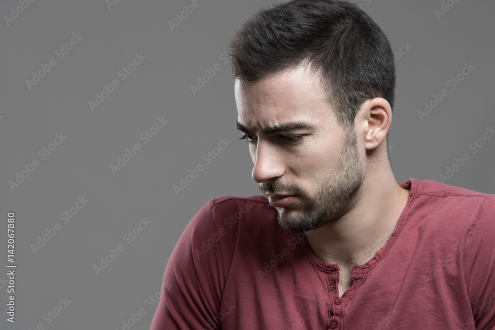 Moody portrait of worried upset man with intense look down over gray studio background. Moody portrait of worried upset man with intense look down over gray studio background.