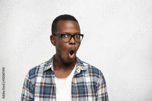 Attractive dark-skinned college student wearing trendy glasses in black frame isolated on white background with copy space for your information, looking shocked, with mouth opened for saying: No way!