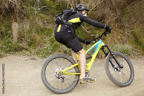 People, active healthy lifestyle, extreme and risk concept. Male Caucasian cyclist wearing stylish cycling clothing and protective gear riding his yellow bicycle on trail in city park or forest