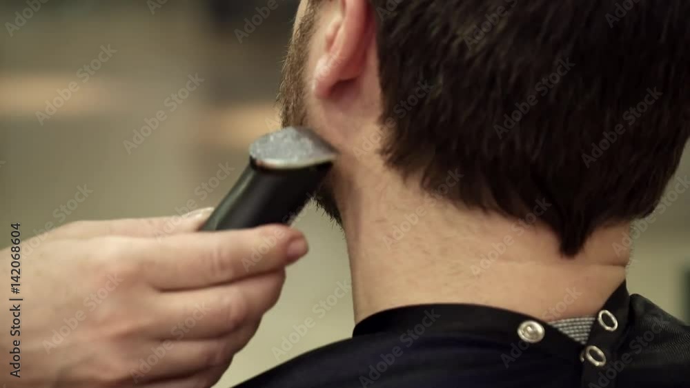 Young man is having his beard cut, view from back Young man is having his beard cut, view from back