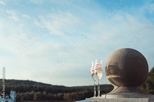 Two wedding champagne glasses with a bow on a stone railing. Lake promenade at sunset