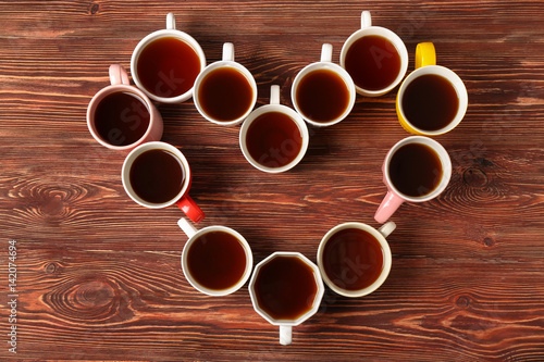 Delicious tea in cups forming heart on wooden background