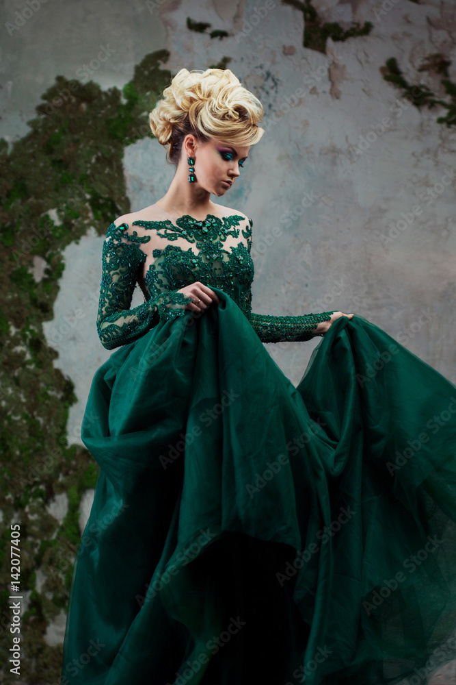 Portrait of young attractive blonde woman in a beautiful green dress. Textured background, interior. Luxury hairstyle