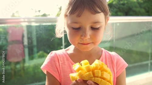 Close-up of 5 year old girl girl eating ripe cut into strips mango.
