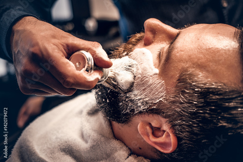 Barber applies shaving foam to a man's face in a saloon. photo