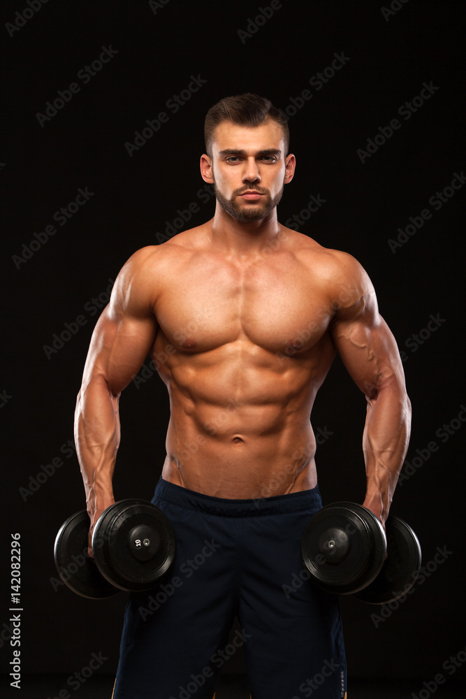 Muscular handsome man is training with dumbbells in gym. isolated on black background with copyspace