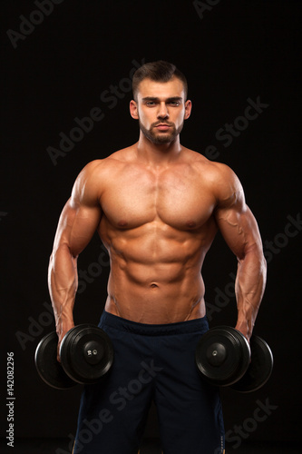 Muscular handsome man is training with dumbbells in gym. isolated on black background with copyspace